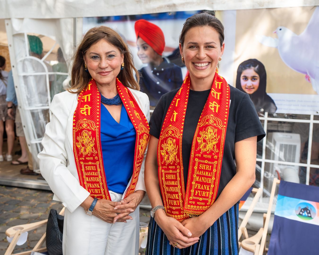 Zwei Frauen mit rot-goldenen Schals an einem Infostand beim Tag der Religionen